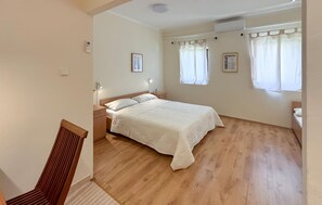 Ein Schlafzimmer mit Holzboden, einem Bett mit weißer Bettdecke, einem Nachttisch und einer Wandleuchte.