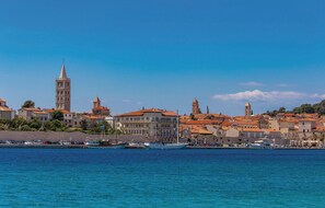 Un pueblo costero con edificios históricos, una torre destacada y un puerto deportivo con barcos.