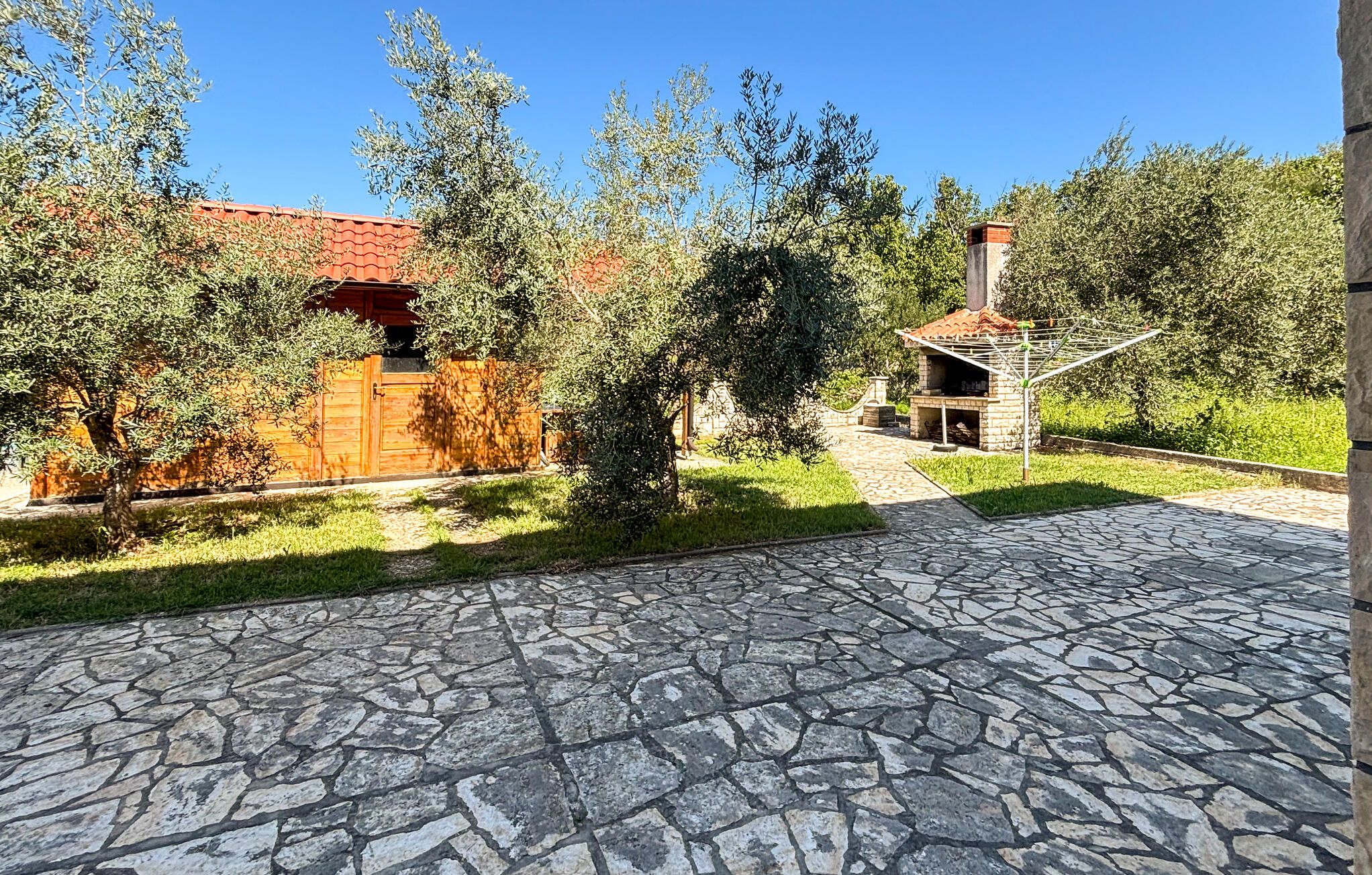 Une cour dallée de pierres, avec un chalet en bois et un espace barbecue en briques.