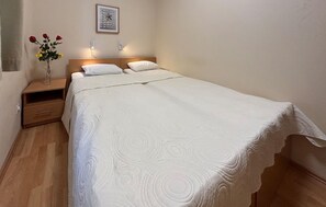 A neatly made bed with a white duvet and pillows, a bedside table with a vase of flowers, and a wall clock. - Lovely apartment in Rab with WiFi (Rab)
