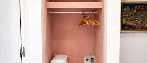 Un armario rosa con barra para colgar ropa, un estante con toallas dobladas y una caja fuerte pequeña.