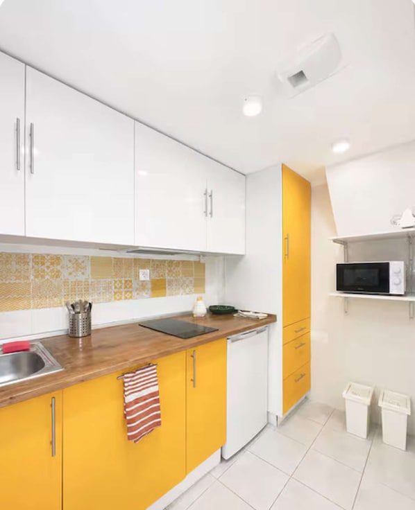 A kitchen with white and yellow cabinets, a stainless steel sink, a microwave, and a dish rack. - Charming Retreat in the Heart of Lisbon (Lisbon)