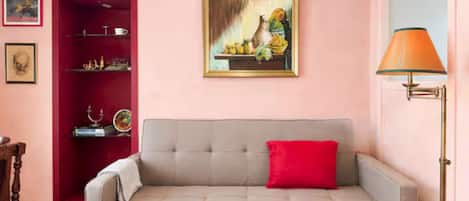 Un salon avec un canapé, un coussin rouge, un tableau, une lampe et un tapis à motifs.