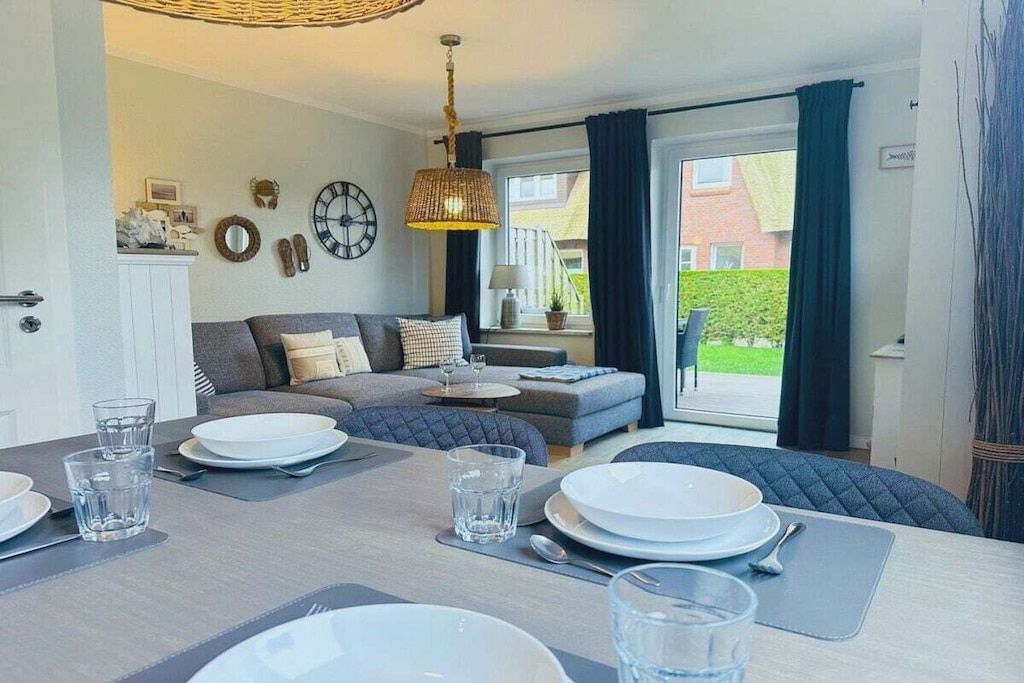 A dining area with a table set for four, a sofa in the background, and a view of the outside.