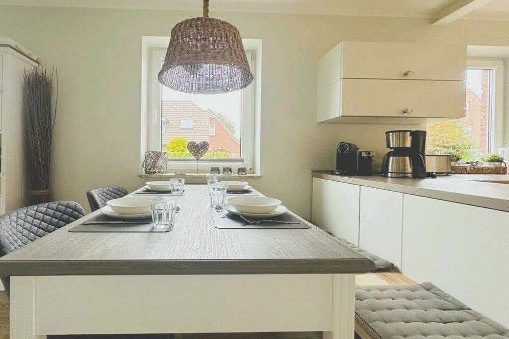 A dining area with a table set for four, a hanging light fixture, and a window with a view of a house.