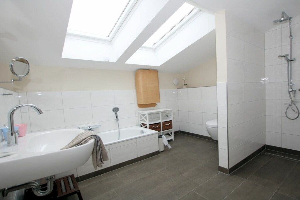 A modern bathroom with a skylight, a bathtub, a toilet, and a shower.