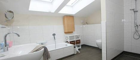 A modern bathroom with a skylight, a bathtub, a toilet, and a shower.