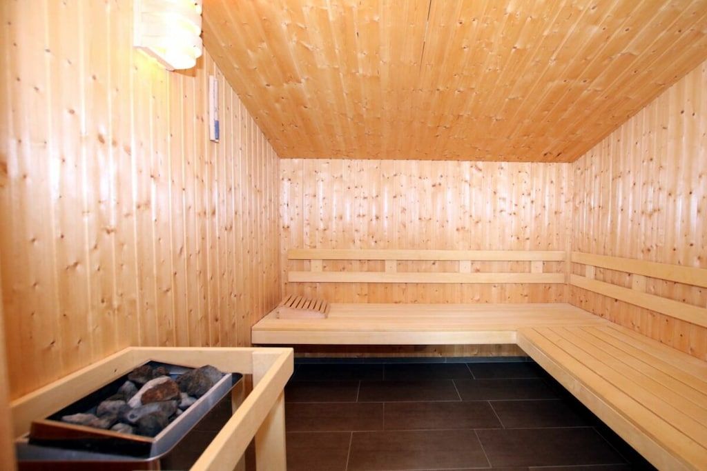 Un sauna avec des bancs en bois et un banc en pierre, un plafond en bois et un sol carrelé.