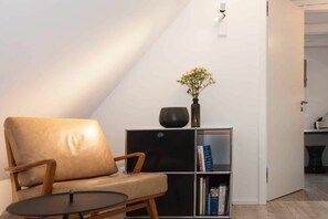 A room with a leather chair, a small table, a bookshelf, and a vase with flowers. - Sonnengold Apartment Sonnengold (St. Peter-Ording)