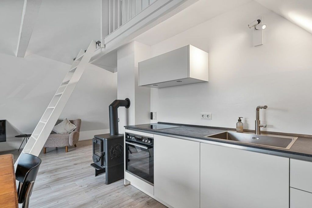 A modern kitchen with a built-in stove, a large island with a sink, and a staircase leading to an upper level.