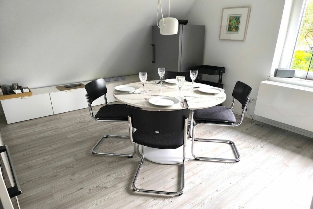 Een moderne eethoek met een ronde tafel, zwarte stoelen en een witte hanglamp.