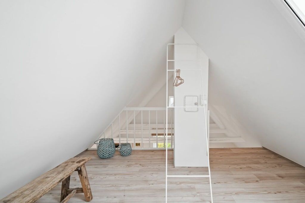 A minimalist room with a sloped ceiling, a wooden bench, and a white storage unit.