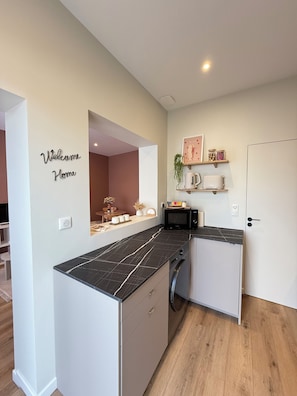 A modern kitchen with a black marble countertop, a washing machine, and a microwave. - Bright house for two, 200 m from the sea (Fouras)