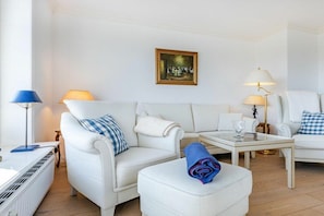 Ein modernes Wohnzimmer mit weißen Möbeln, einem Gemälde an der Wand und zwei Lampen.