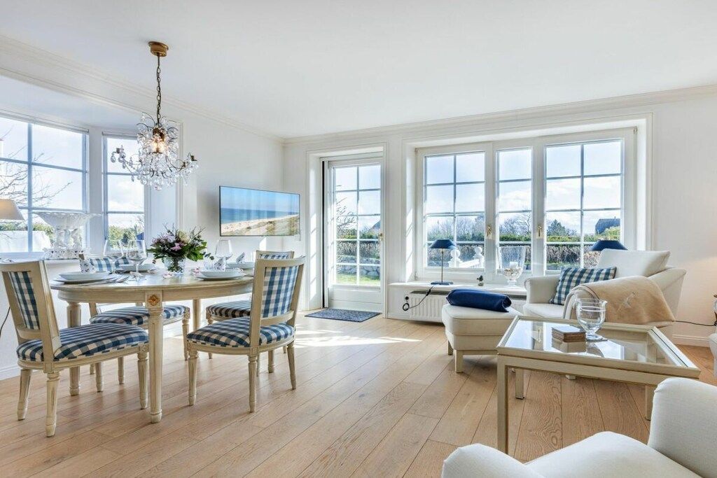 A dining area with a round table, chairs, and a chandelier. There is a sofa and a coffee table in the living area.