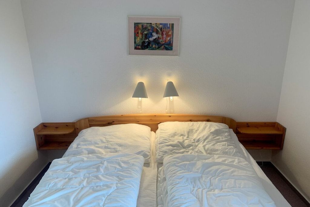 Un lit double avec deux tables de chevet, un tableau abstrait encadré au-dessus, et deux lampes fixées au mur.