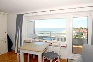 Ein Zimmer mit Holztisch und -stühlen, Meerblick und einem Balkon mit Geländer.