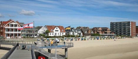 A beachside promenade with a wooden walkway, beach umbrellas, and buildings in the background.