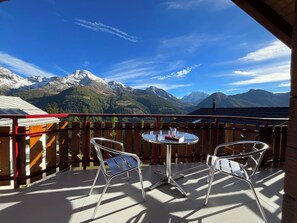 Ein Balkon mit zwei Stühlen und einem Tisch, mit Blick auf eine gebirgige Landschaft.