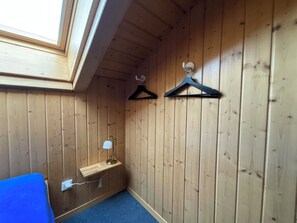 Ein Eckzimmer mit Holzwänden, einem Oberlicht, einem Schreibtisch mit Lampe und zwei Wandhaken.