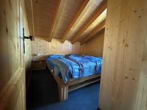 Ein Zimmer mit Holzboden, einem Einzelbett, einem kleinen Tisch und einer Tür.