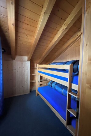Ein Zimmer im Dachgeschoss aus Holz mit Etagenbett und geneigter Decke.