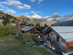 Eine Berglodge mit Holzfassade, einer überdachten Außenbereich-Sitzgelegenheit und Blick auf schneebedeckte Berge.