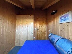A room with wooden walls, a bed with a blue mattress, a wall-mounted heater, and a painting. - Schirli Dachgeschoss Appartement/Fewo, Bad, WC 6-Bettwohnung by Interhome (Rosswald)