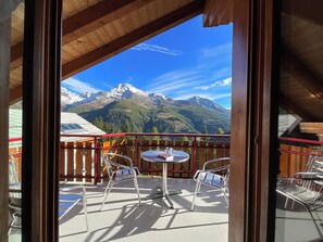 Ein Balkon mit Blick auf schneebedeckte Berge, ein runder Tisch mit Stühlen und ein Holzzaun.