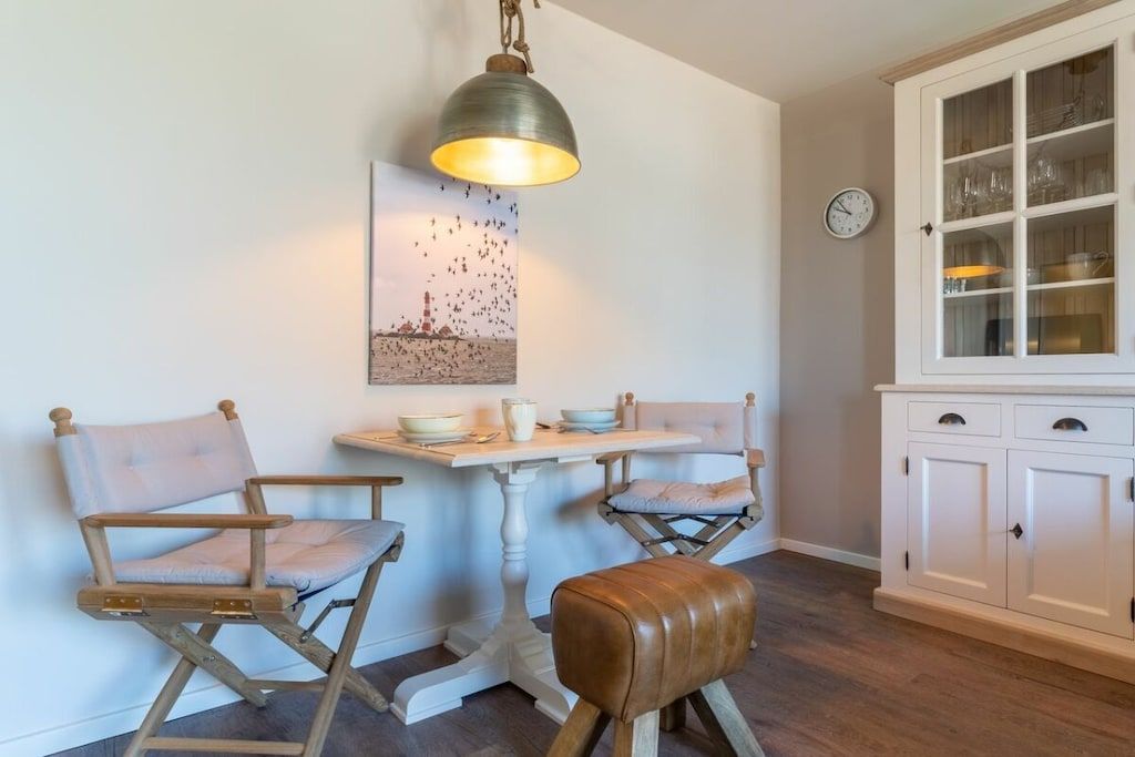 Un coin repas comprenant deux chaises, une table, un banc, un luminaire suspendu, une horloge murale et un meuble avec des portes en verre.