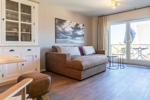 A modern living room with a sofa, a cabinet with glass doors, a painting, and a balcony with outdoor furniture. - Holiday apartment with 1 bedroom (St. Peter-Ording)