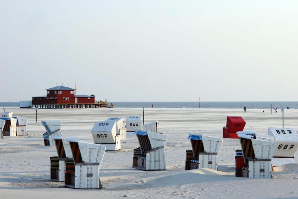 Beach chairs numbered 807, 844, and 887 on a sandy beach with a lifeguard tower in the background.