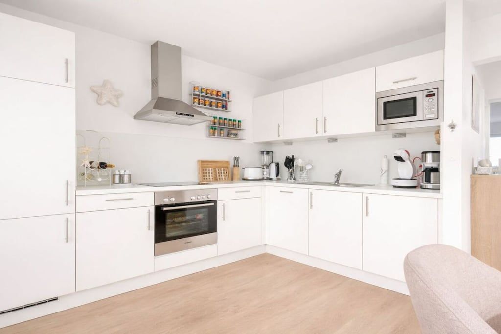 Een moderne keuken met witte kastjes, een roestvrijstalen oven, een magnetron en een koffiezetapparaat.