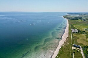 Eine Luftaufnahme einer Küstenregion mit Strand, klarem Wasser und angrenzenden grünen Feldern.
