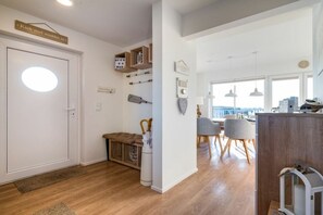 Ein modernes Interieur mit Holzboden, einer Bank, einem Essbereich mit Stühlen und einer weißen Tür mit rundem Fenster.
