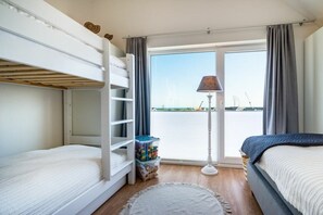 Een kamer met stapelbedden, een lamp, uitzicht op het water en een opbergruimte.