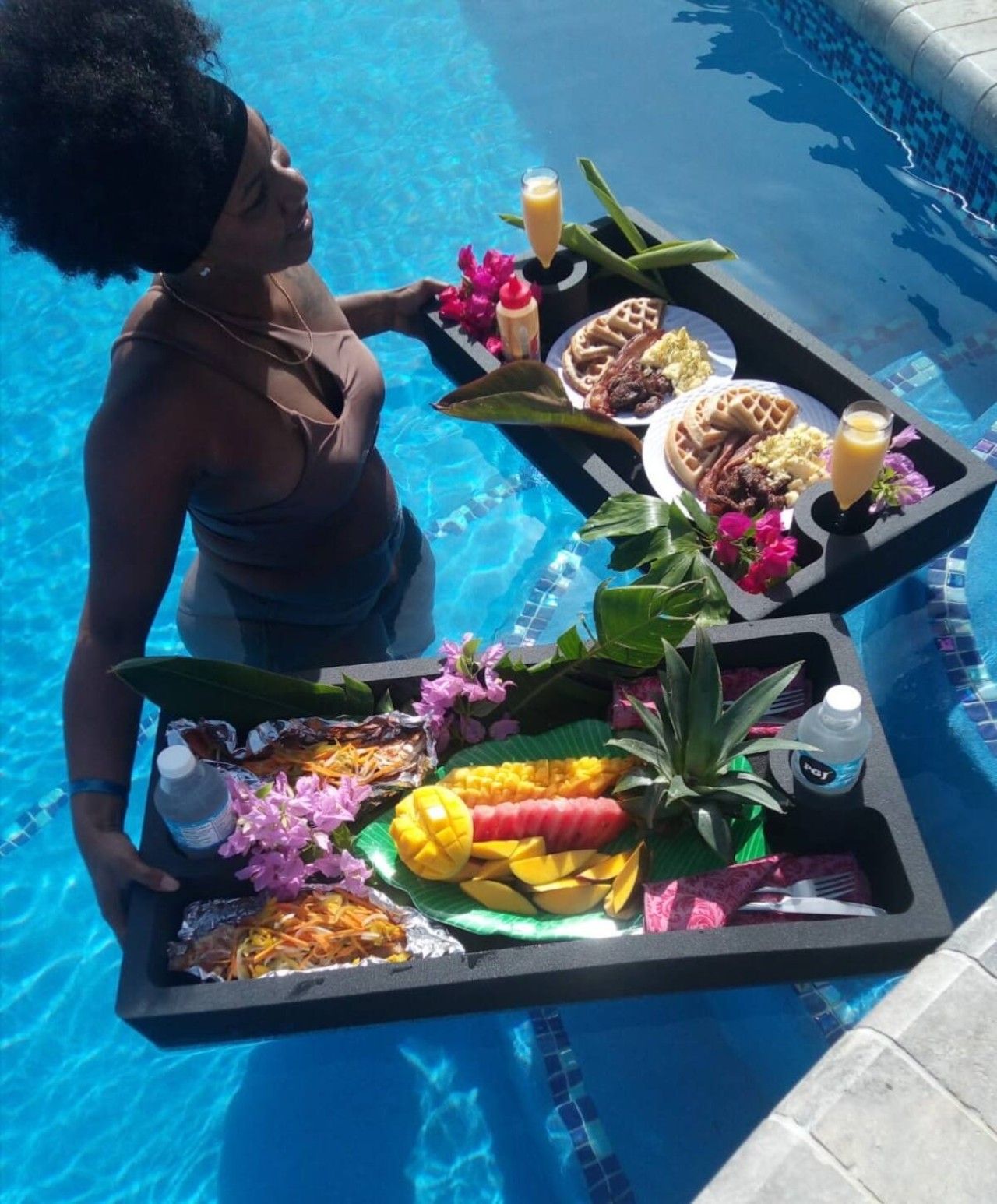 A person holding a tray with food and drinks by a pool.