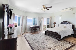 A bedroom with a bed, a desk, a chair, a ceiling fan, and a view of the outdoors. - Hospitality Expert VSV GF 3BR - Chef, Pool, Beach (Montego Bay)