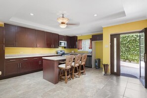 A kitchen with dark wooden cabinets, a central island with bar stools, a microwave, and a stove. - Hospitality Expert VSV BF 3BR - Chef, Pool, Beach (Montego Bay)