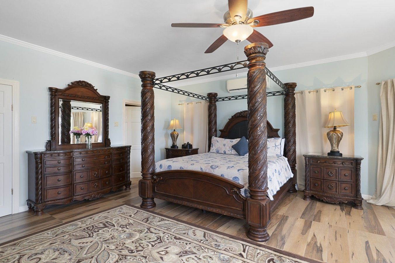 A four-poster bed with a ceiling fan, a large mirror, and a nightstand with a lamp.