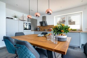 Una cocina moderna con una mesa de comedor de madera, sillas azules y lámparas colgantes de cobre.