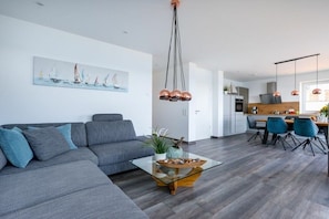 A modern living room with a grey sofa, a glass coffee table, and a dining area with chairs. - Holiday apartment with 2 bedrooms (Kappeln)
