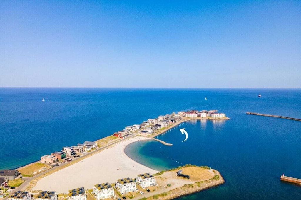 An aerial view of a coastal area with a sandy beach, a marina, and several buildings.