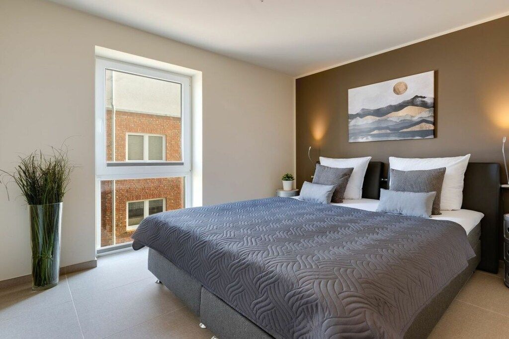 Ein Schlafzimmer mit einem großen Bett, einem Fenster, einem Gemälde und einer Pflanze.