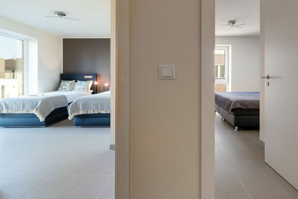 A hotel room with two beds, a large window, and a door leading to another room.