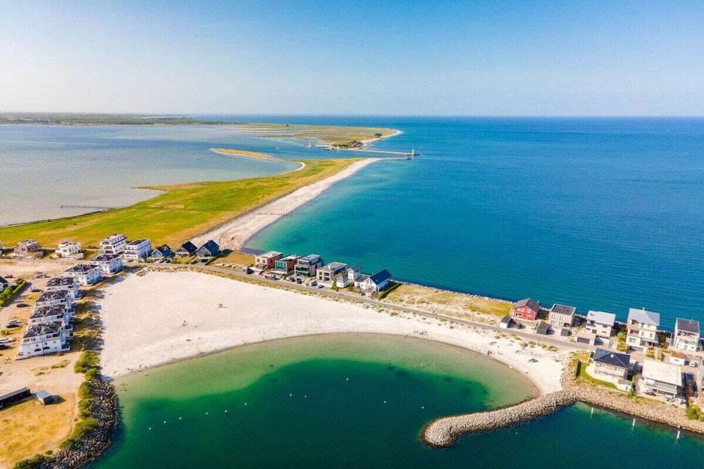 Une propriété située sur la côte, avec une plage, un port de plaisance et un phare visible au loin.