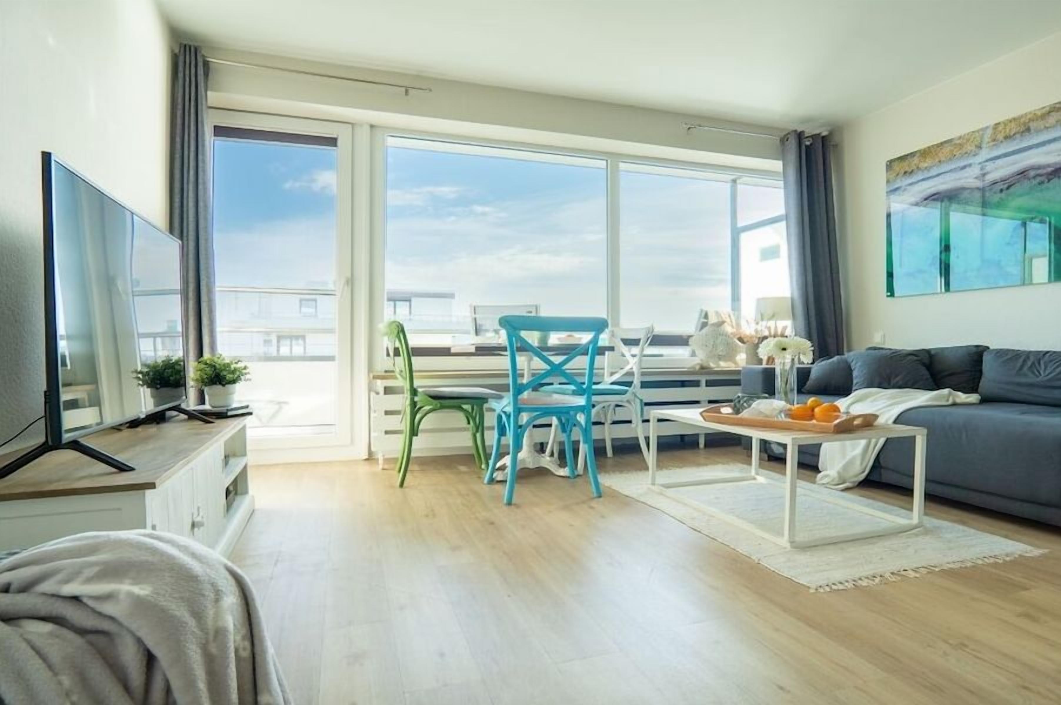 Een moderne woonkamer met een bank, een salontafel en twee stoelen. Er is een televisie op een meubel en een raam met uitzicht op de stad.