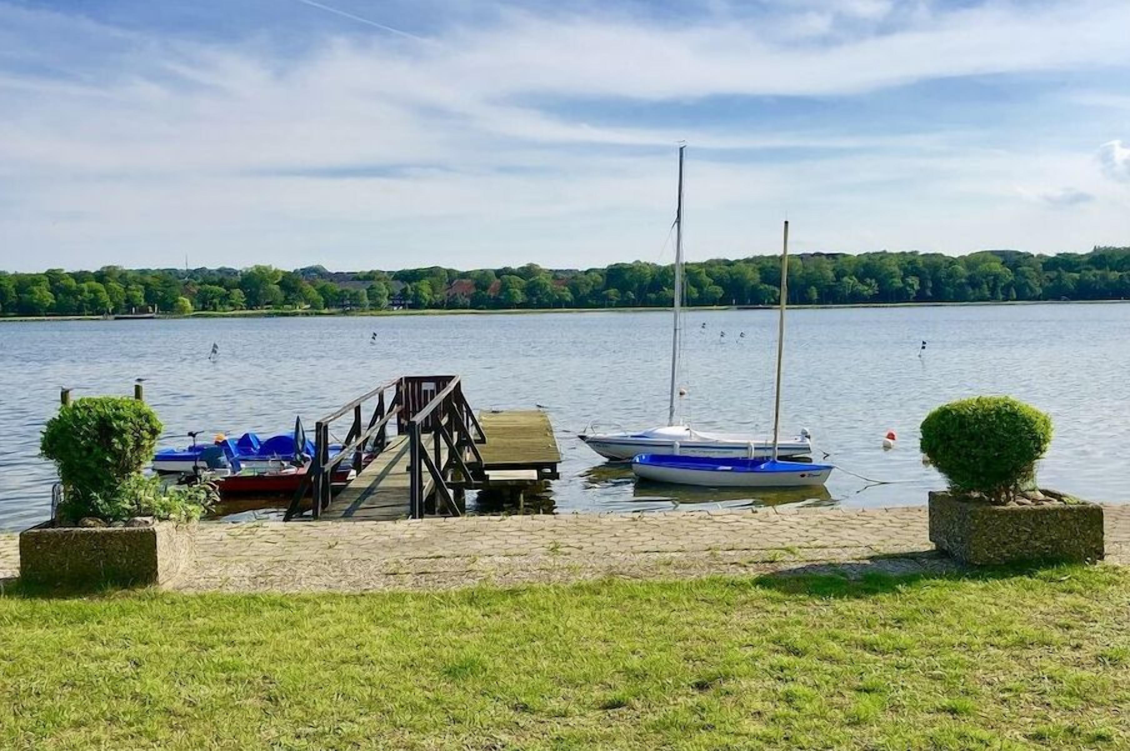 A calm lake with docked boats, a wooden pier, and a clear sky.
