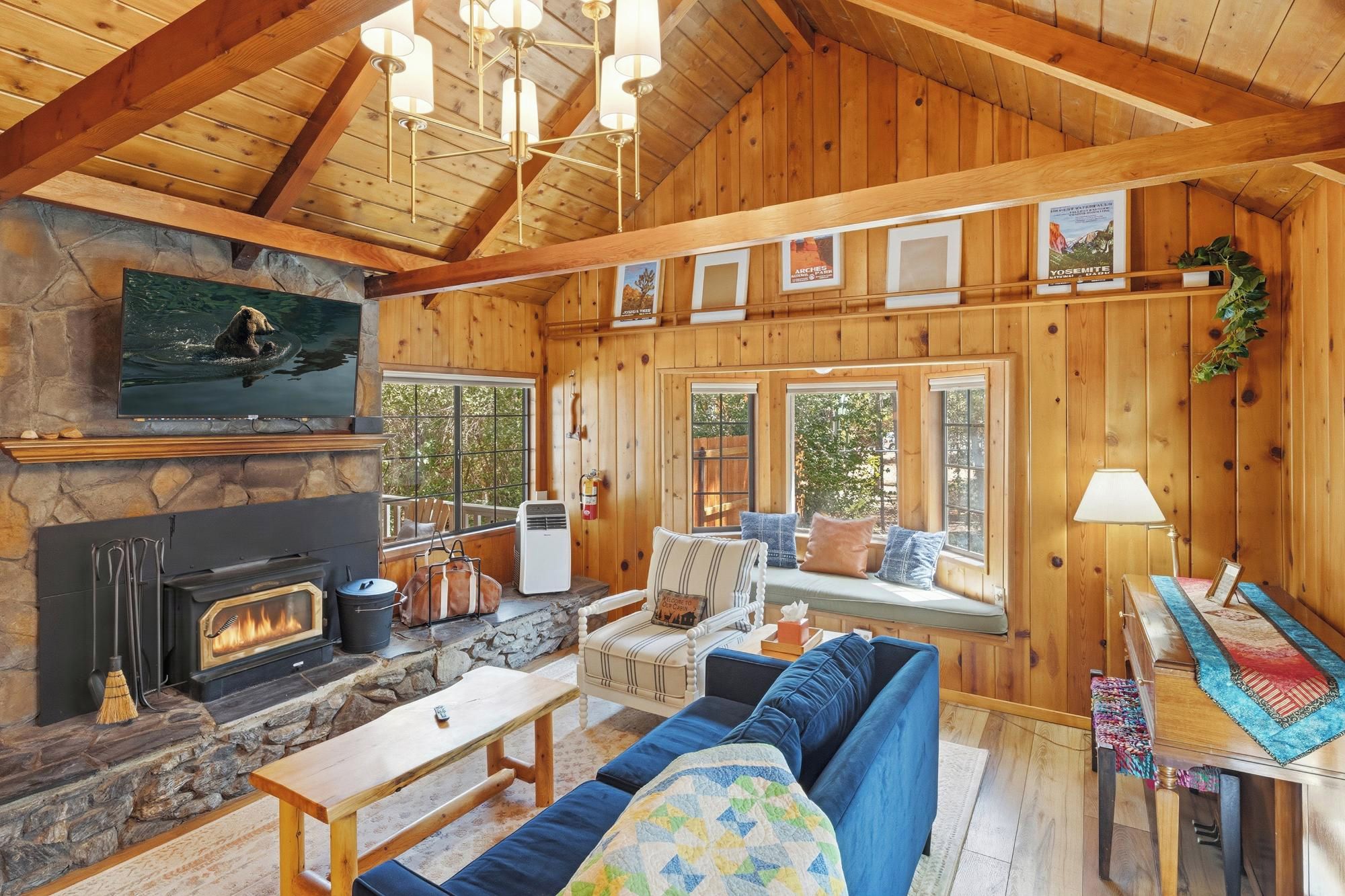 A cozy cabin interior with a stone fireplace, a television mounted above it, and a comfortable seating area with a blue sofa and a wooden table.