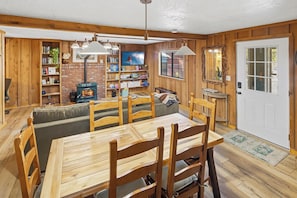 A cozy wooden interior with a dining table, chairs, a sofa, a fireplace, and bookshelves. - HOT TUB! PET FRIENDLY! Basketball! Fire Pit! EV Charger! A/C! (Big Bear City)